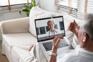 An older man is sitting on his couch, getting an online medical second opinion from a physician.