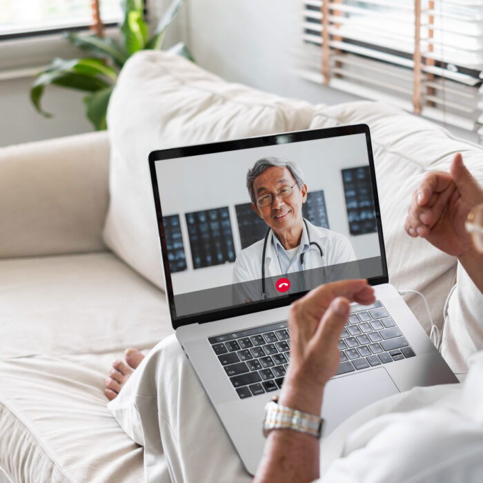 An older man is sitting on his couch, getting an online medical second opinion from a physician.