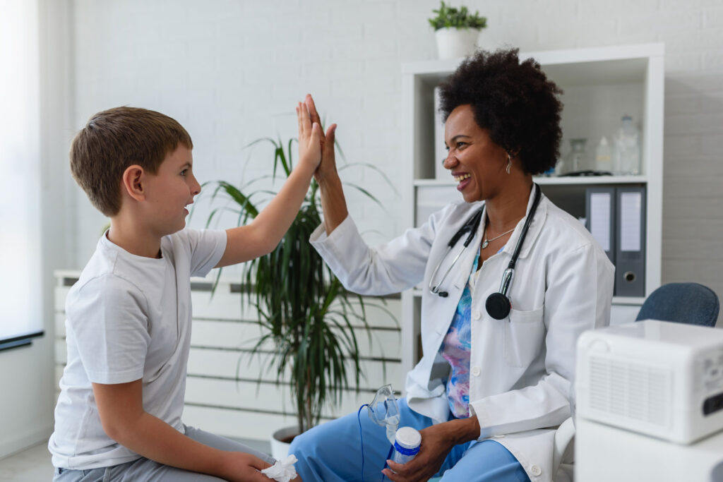 A little boy and a doctor are high-fiving during his exam. He is thriving after a virtual second opinion.