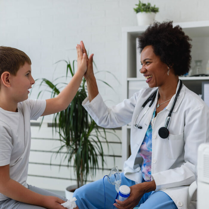 A little boy and a doctor are high-fiving during his exam. He is thriving after a virtual second opinion.